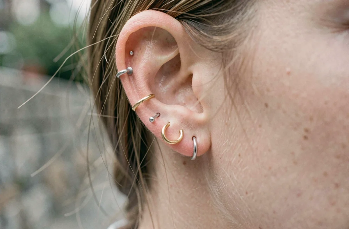 Gros plan sur une oreille avec sept piercings en constellation mêlant or et argent, arrangement harmonieux et minimaliste
